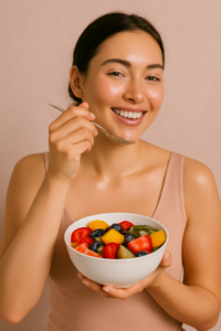 Woman eating a colorful bowl of fruit, smiling with glowing skin